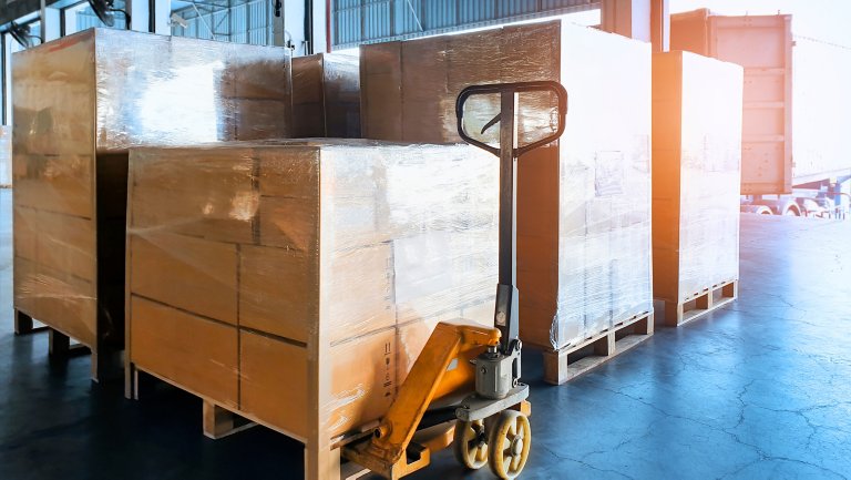 Cardboard boxes wrapped in plastic and stacked on hand cart in warehouse