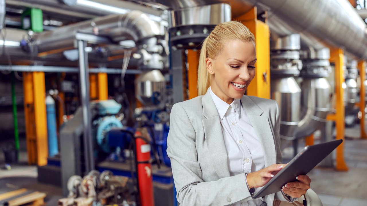Smiling female standing in heating plant and using tablet to check on machinery.