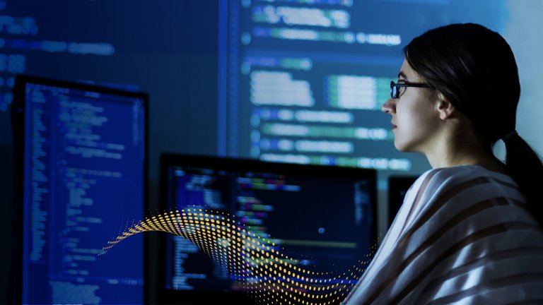 Professional female technology expert sitting in front of multiple computer screens showing software code