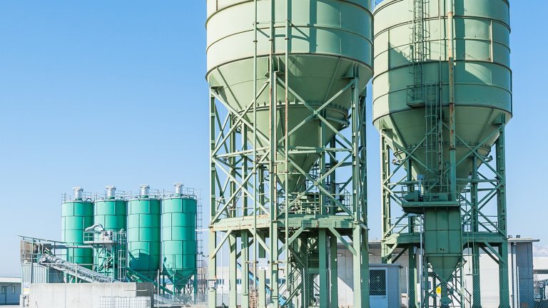 Dois grandes silos de armazenamento ao lado de quatro silos de armazenamento menores na fábrica de cimento 