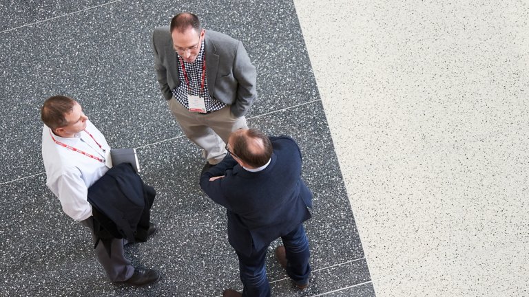 An overhead view looking down on three men dressed in business attire talking to each other.