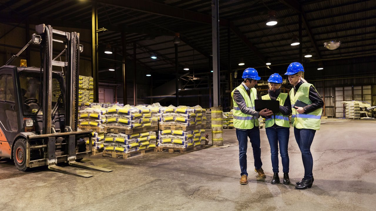 Three workers are standing and looking at a tablet on the manufacturing plant floor 