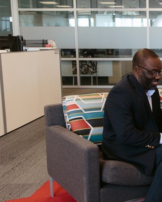 Two diverse employees meet at Rockwell Automation Headquarters. They are sitting on a couch and smiling and looking at a laptop. 