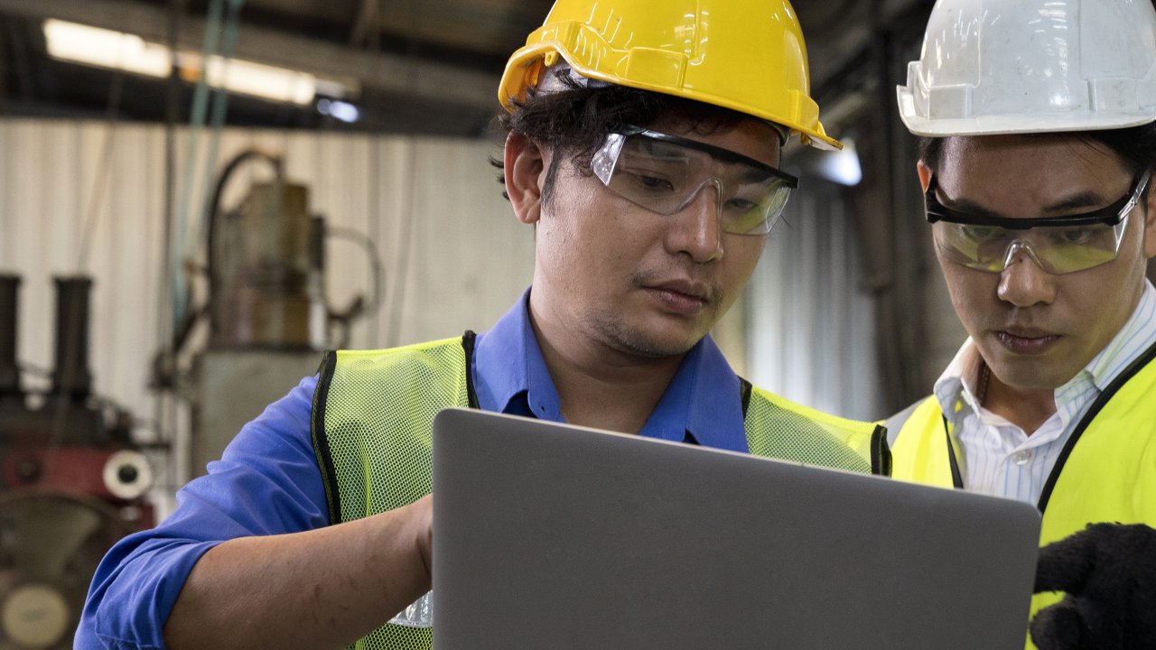 Two men in hard hats holding a laptop on the manufacturing floor