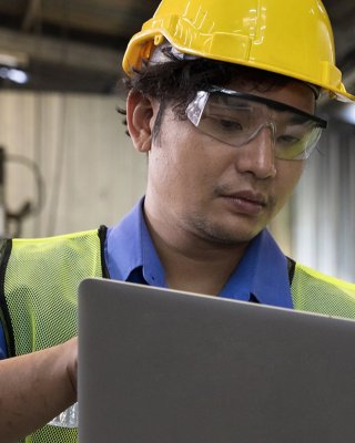 Two men in hard hats holding a laptop on the manufacturing floor