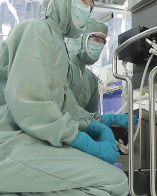 Two life sciences workers in full protective gear connect hoses to a single-use bioreactor bag in a manufacturing facility.