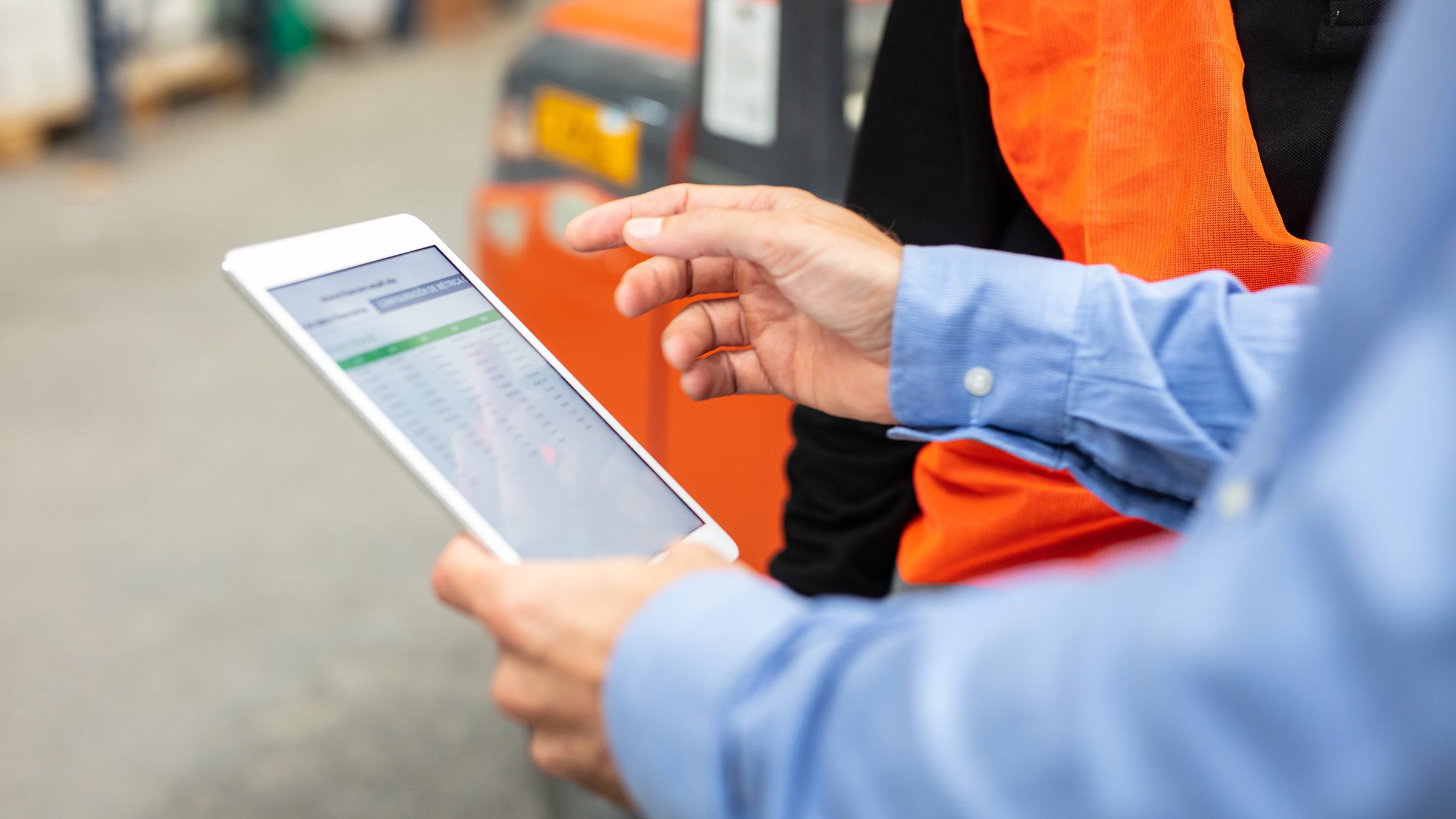 Close-up of a foreman holding digital tablet discussing dispatch plan with the worker in warehouse. Cropped shot of supervisor with tablet pc talking with worker.