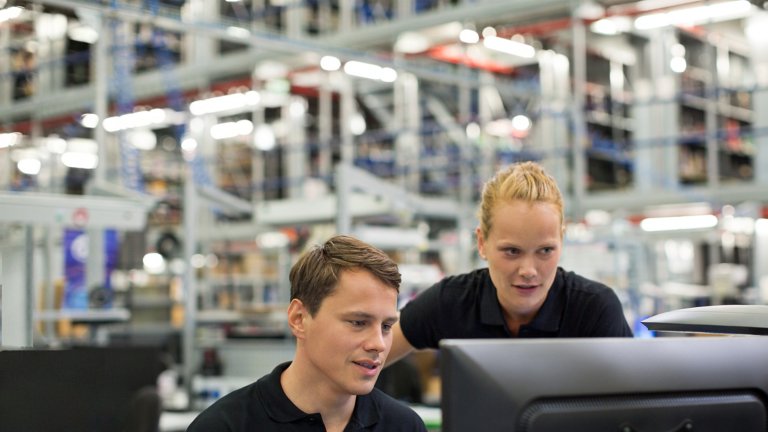 Two employees in a factory viewing data on a monitor