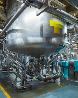 View of factory floor with stainless vertical steel tanks and pipes with pressure meter.