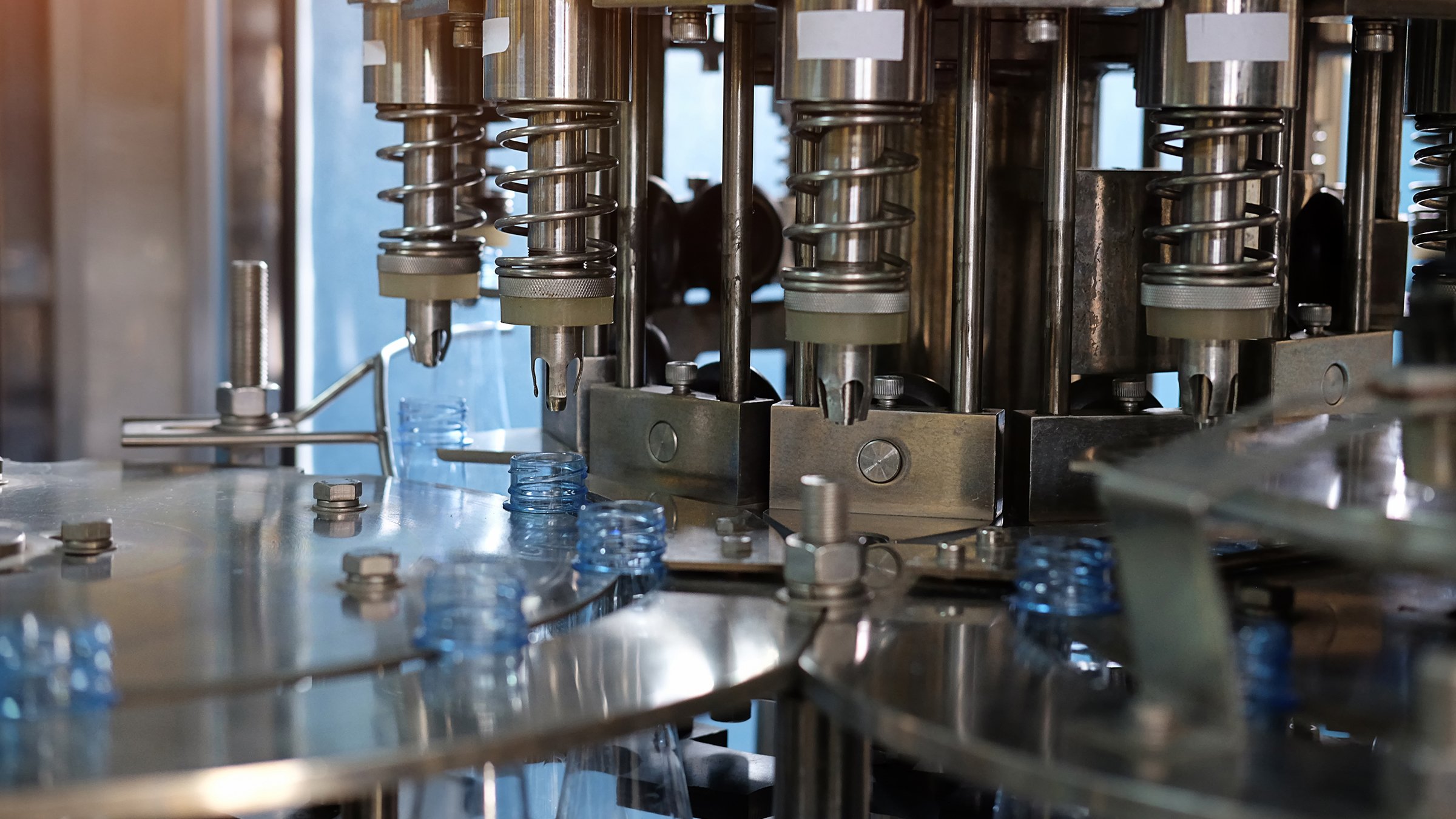 Bottles rotating inside of a machine below a turret that is filling them with water.