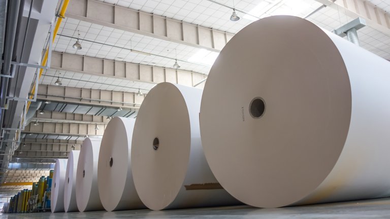 Grandes rolos de papel branco colocados no chão em uma fábrica de papel