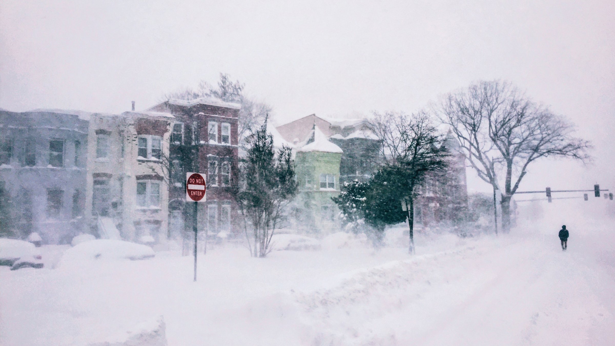 Winter snow scene in neighborhood of homes with a man walking in the street.