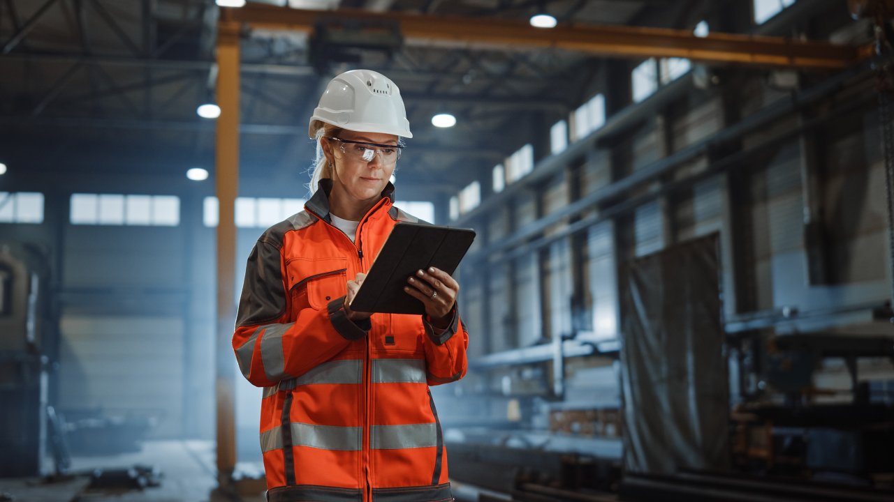 Female engineer in orange jacket looking at tablet in the factory building