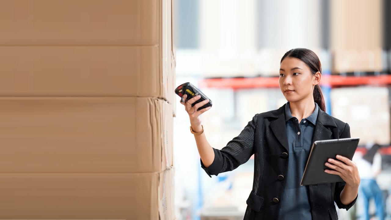 Asian Female Warehouse Staff checking product on-hand by using barcode handheld reader compare with data in an ERP software.