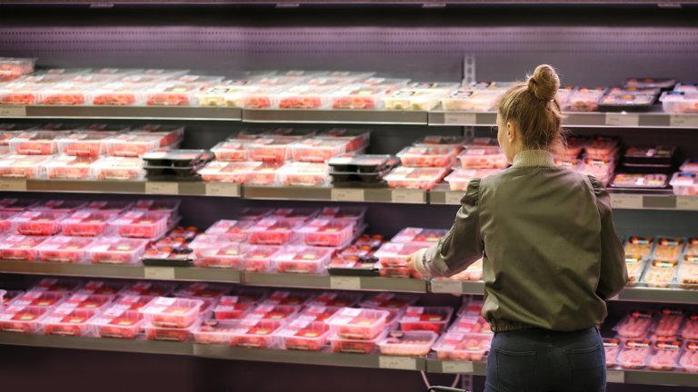 Una mujer de pie frente a un mostrador de carne en una tienda recogiendo un paquete.