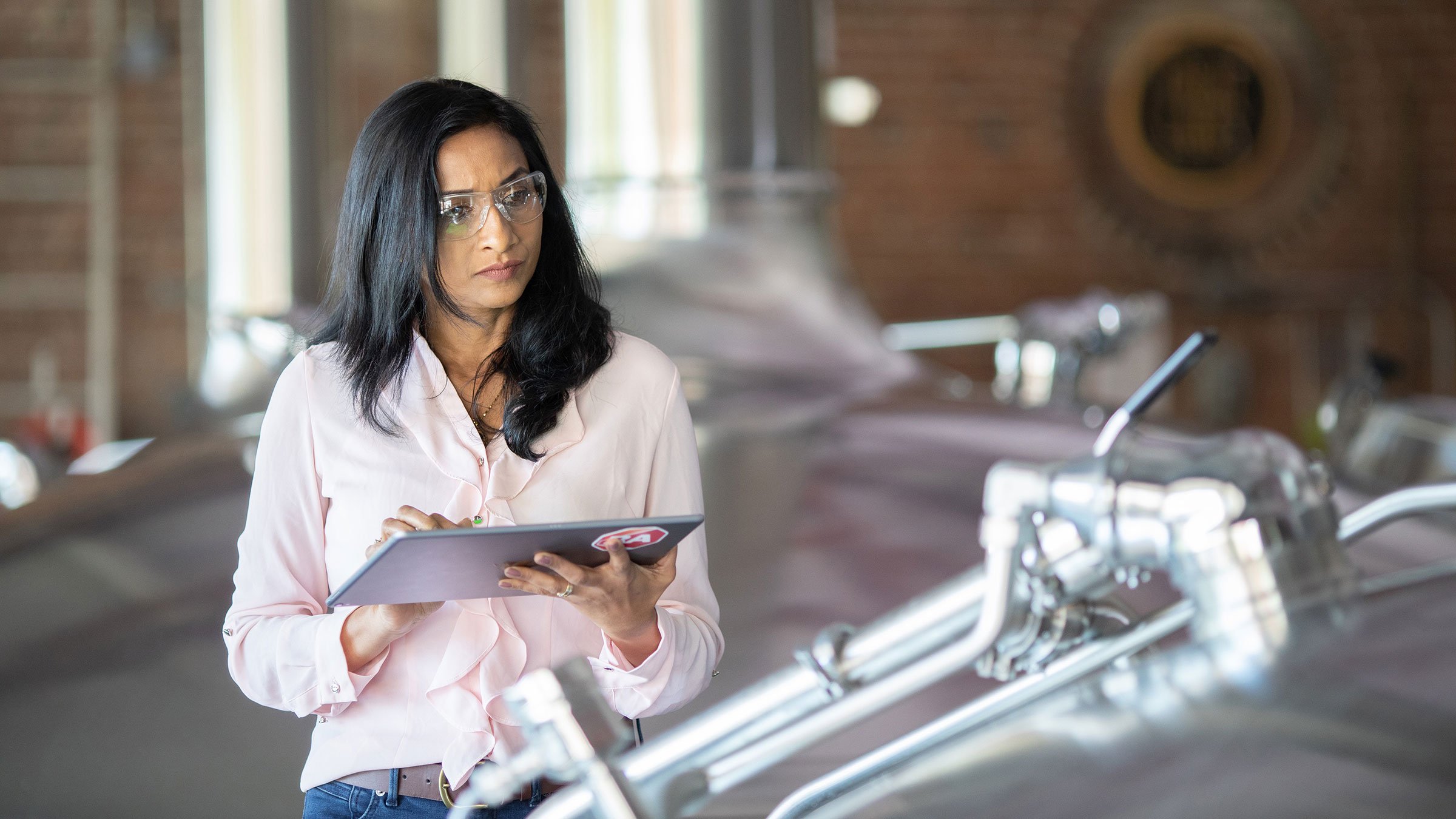 Woman with a safety glasses on is auditing something on her tablet