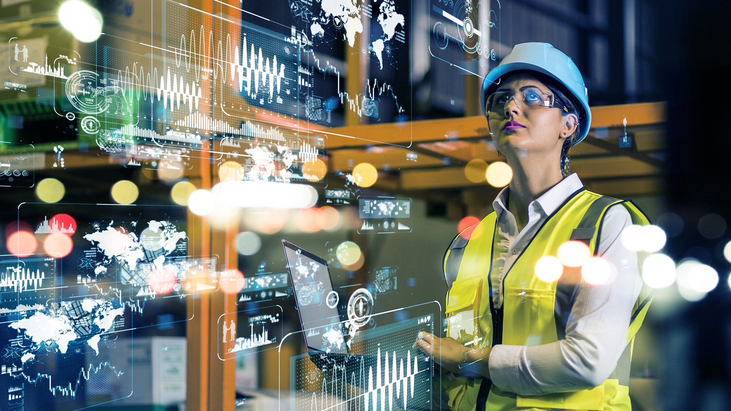 Woman in safety gear using laptop in factory with analytic graphics superimposed over photos