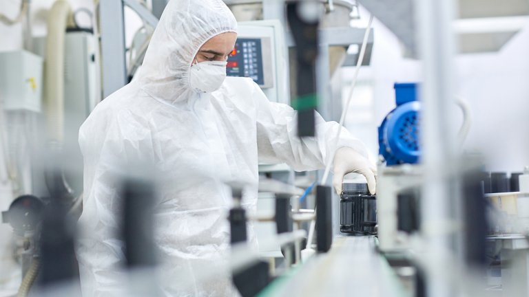 Worker wearing coverall and safety mask working on production line of modern pharmaceutical factory, portrait shot