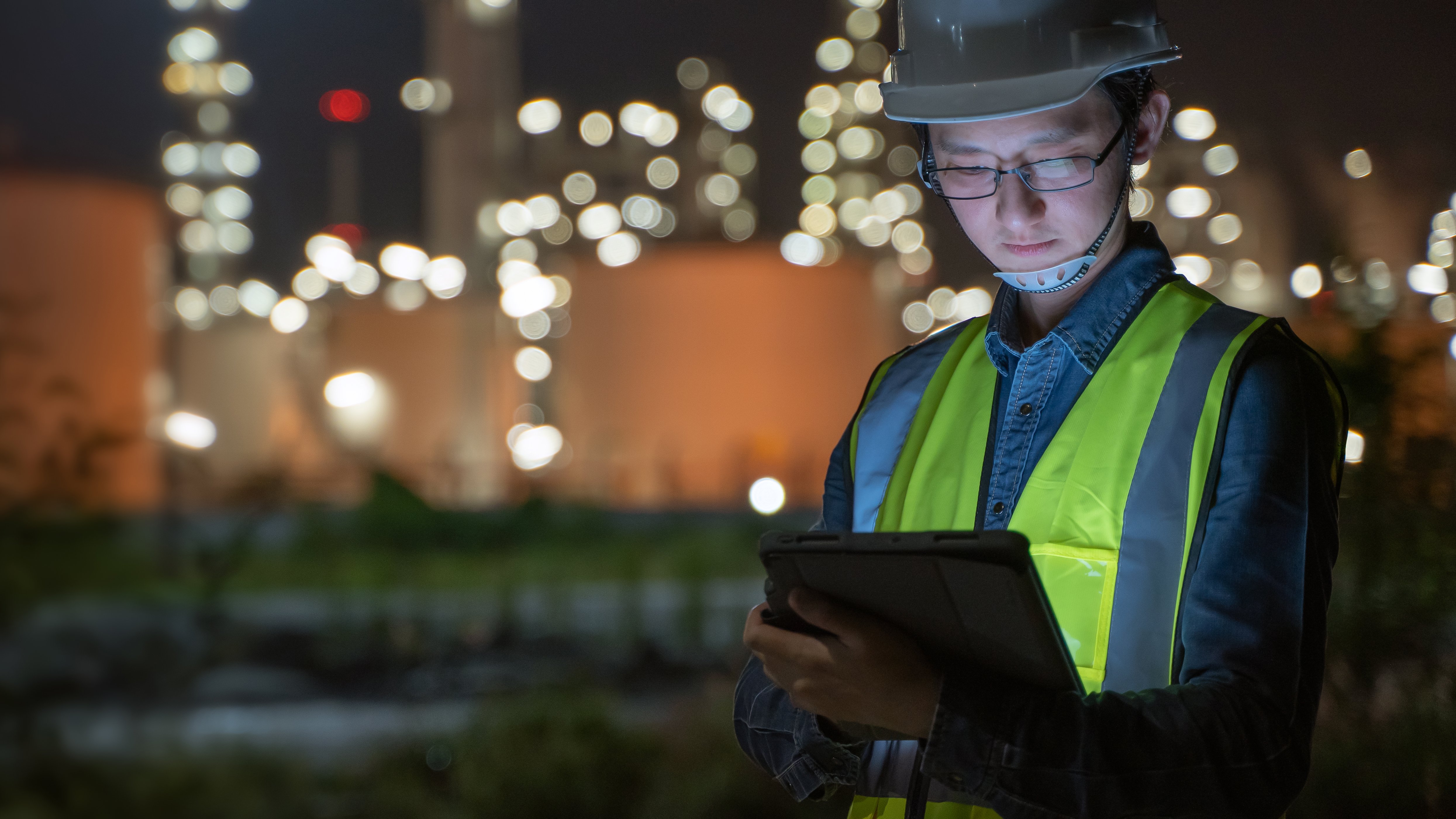 Worker in yellow vest with ipad in dark onsite.