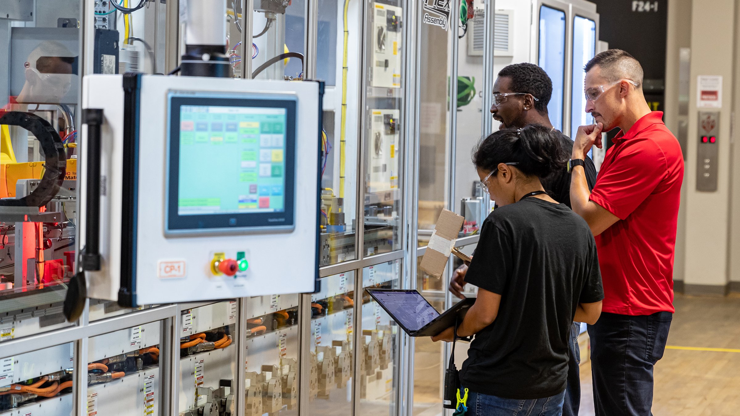 3 workers surrounding a monitor containing GuardLink technology near production line