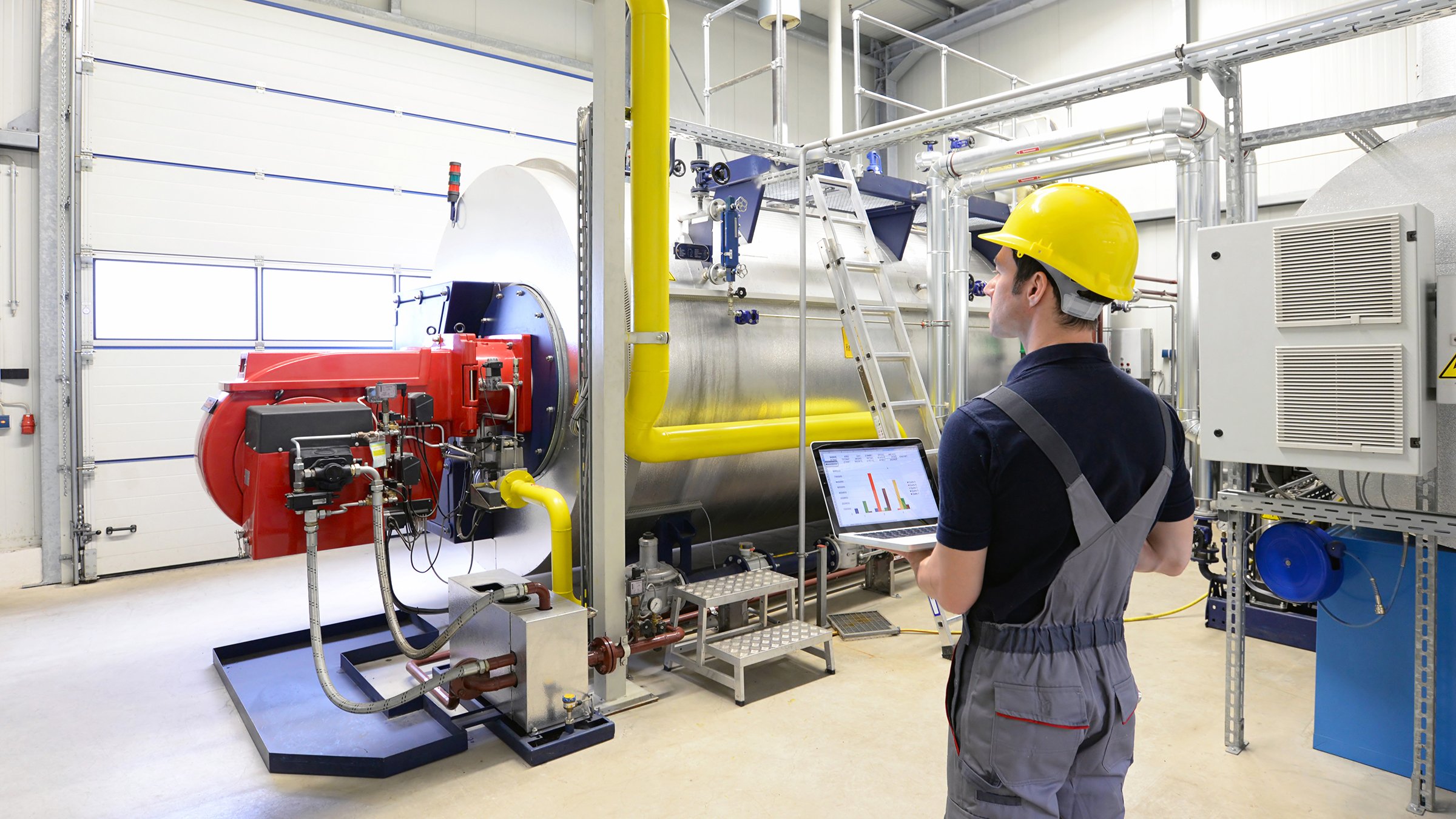 A male worker in yellow hard hat uses modern technology to monitor systems in an industrial manufacturing environment. Worker in an industrial plant check the systems with modern technology