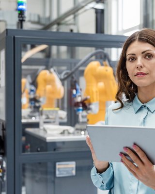 Businesswoman in high tech company controlling industrial robots, using digital tablet