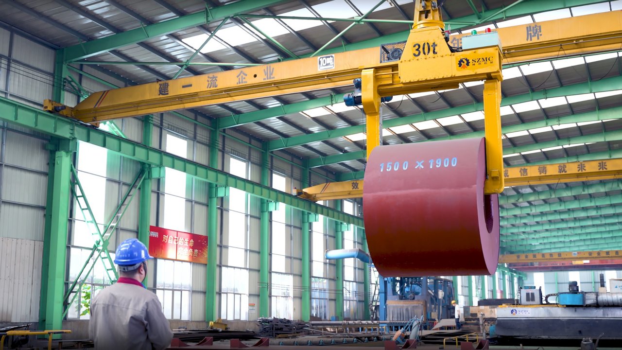 Overhead crane lift up steel coil with tong in wearhouse. Steel coils handling equipment. Steel warehouse and logistics operations.