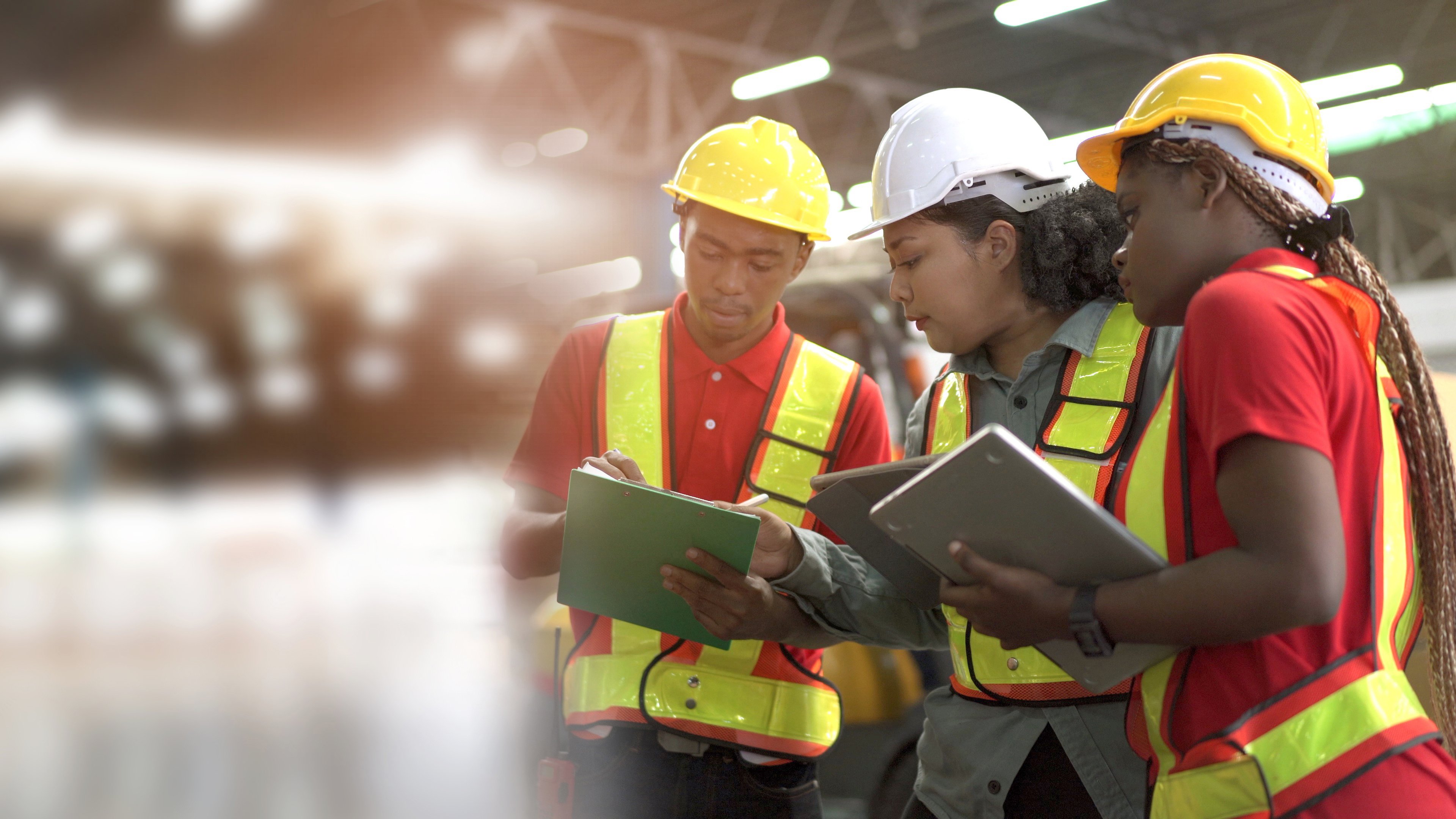 Two women and one man in safety gear. Team of professional engineers or foreman working and discussing together in the factory, Engineer walking around the warehouse to inspect a machines.