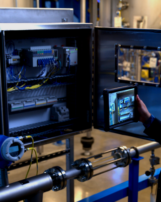Man standing in front of manufacturing control panel is interacting with the equipment using FactoryTalk InnovationSuite Vuforia software and a tablet device.