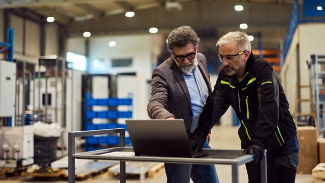 Two men collaborating on a laptop in an industrial setting
