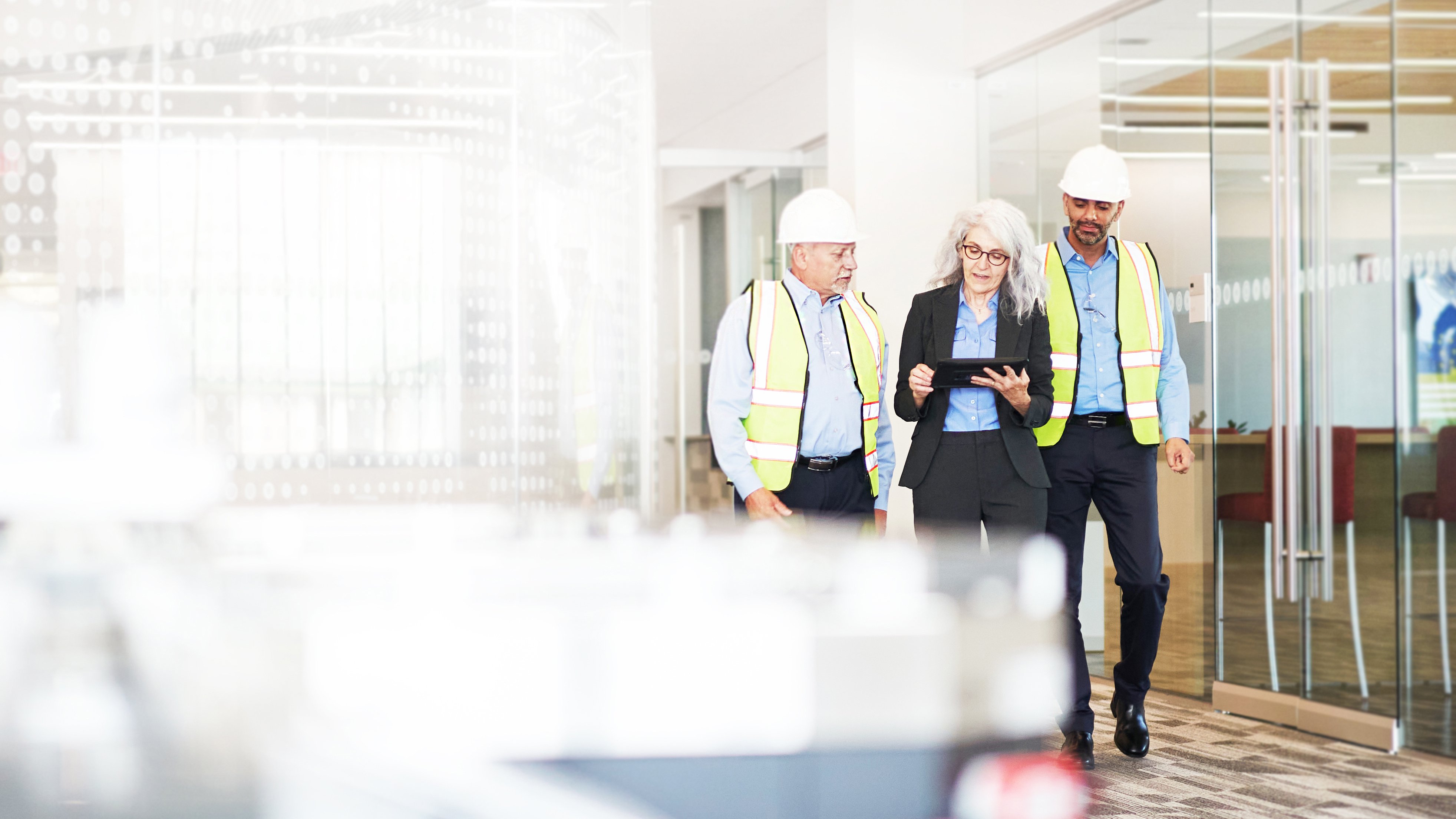 Business person with tablet device sharing information with two colleagues who are wearing hard hats and safety gear