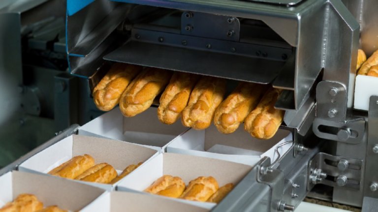 Boxes with eclairs on conveyor. Machine puts eclairs into boxes. Even portions of dessert. Pastry with delicious filling.
