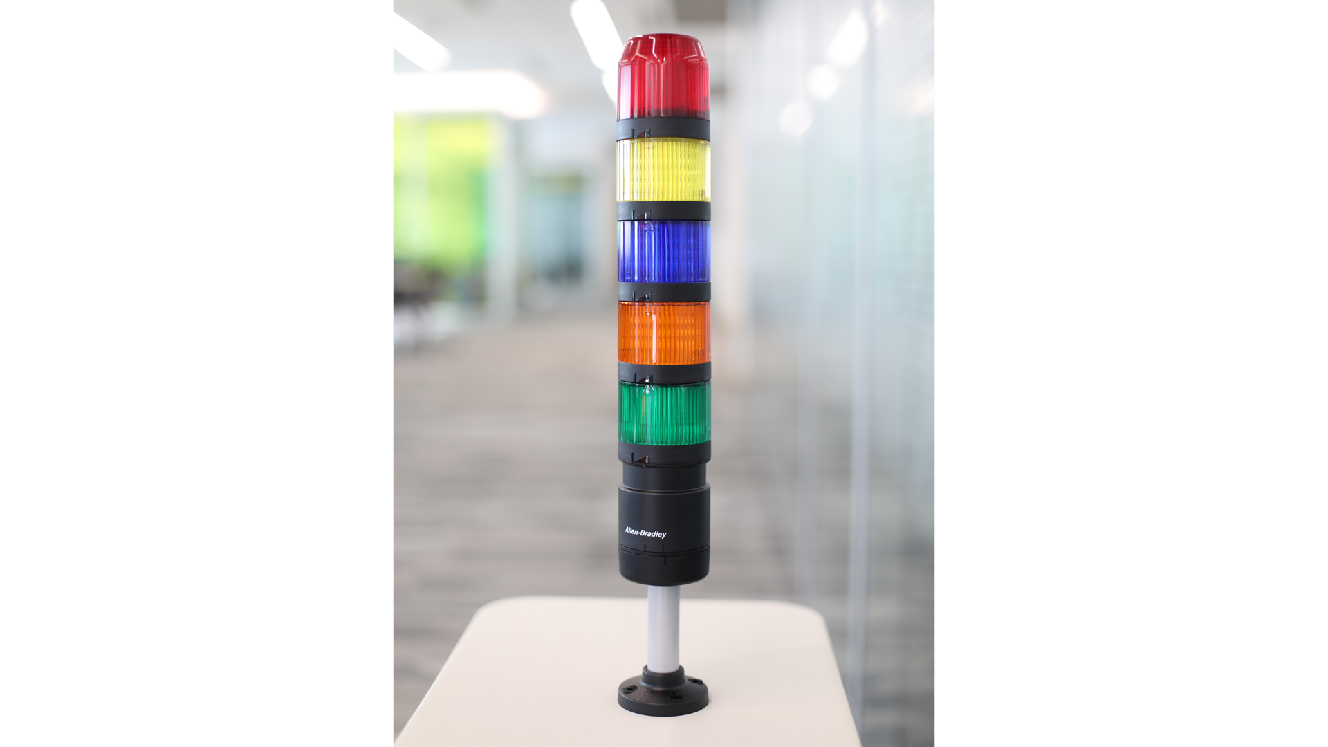 Columna luminosa IO-Link sobre una mesa. De arriba a abajo: módulos de luz rojo, amarillo, azul, ámbar y verde apagados, poste de montaje negro 