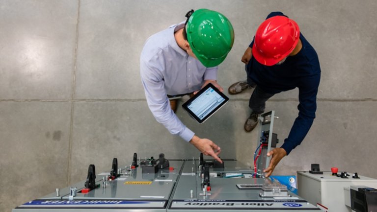Aerial view of two male employees in the factory viewing a tablet in front of a Rockwell Automation product