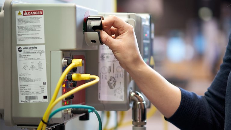 Una mano de mujer pulsando un interruptor en un entorno de fabricación.