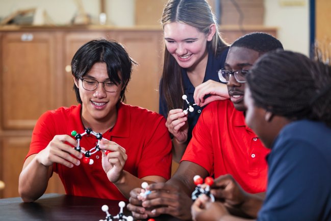 A multiracial group of four high school students in chemistry class examining molecular models together.