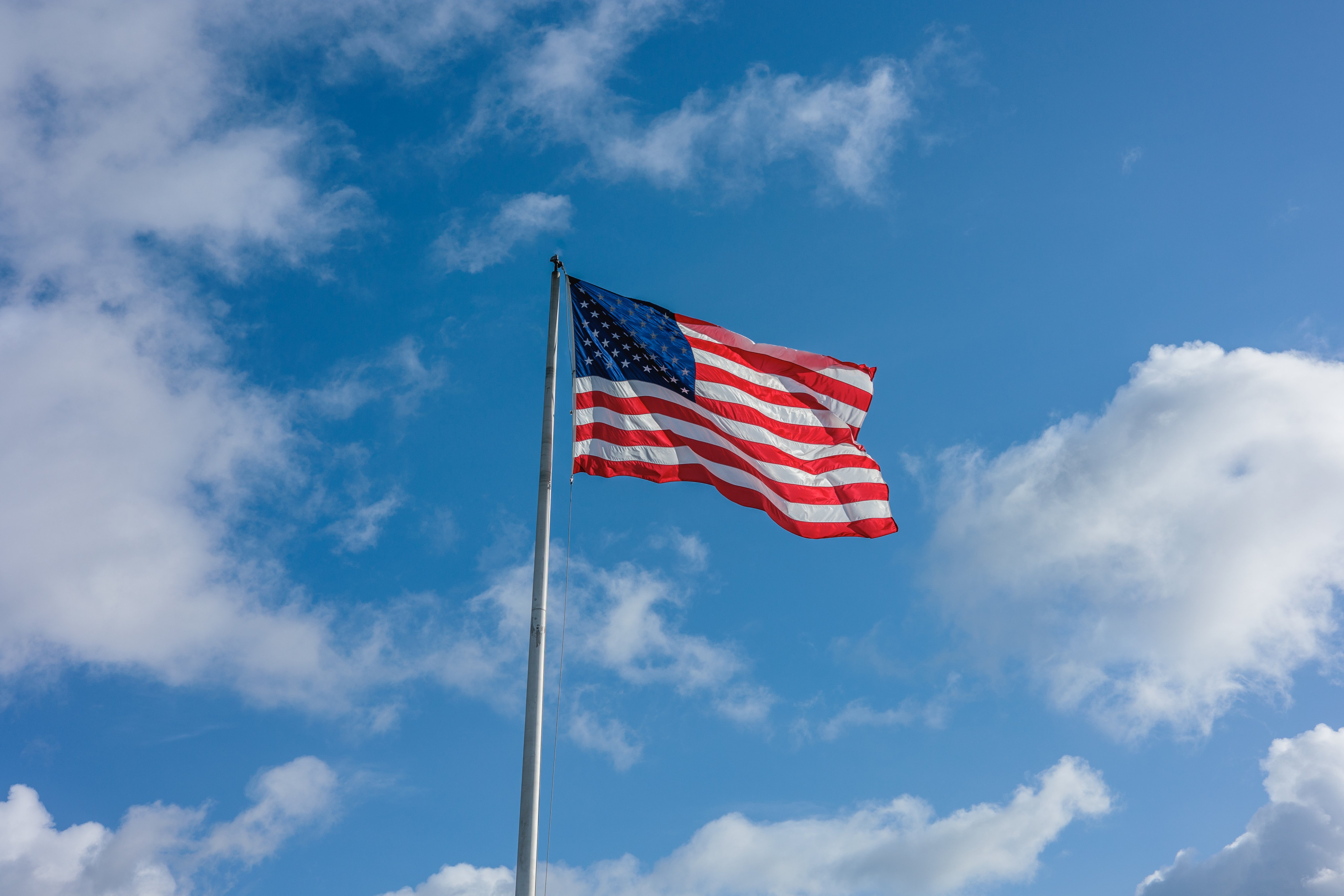 American flag flapping in the wind in front of a blue sky with clouds.