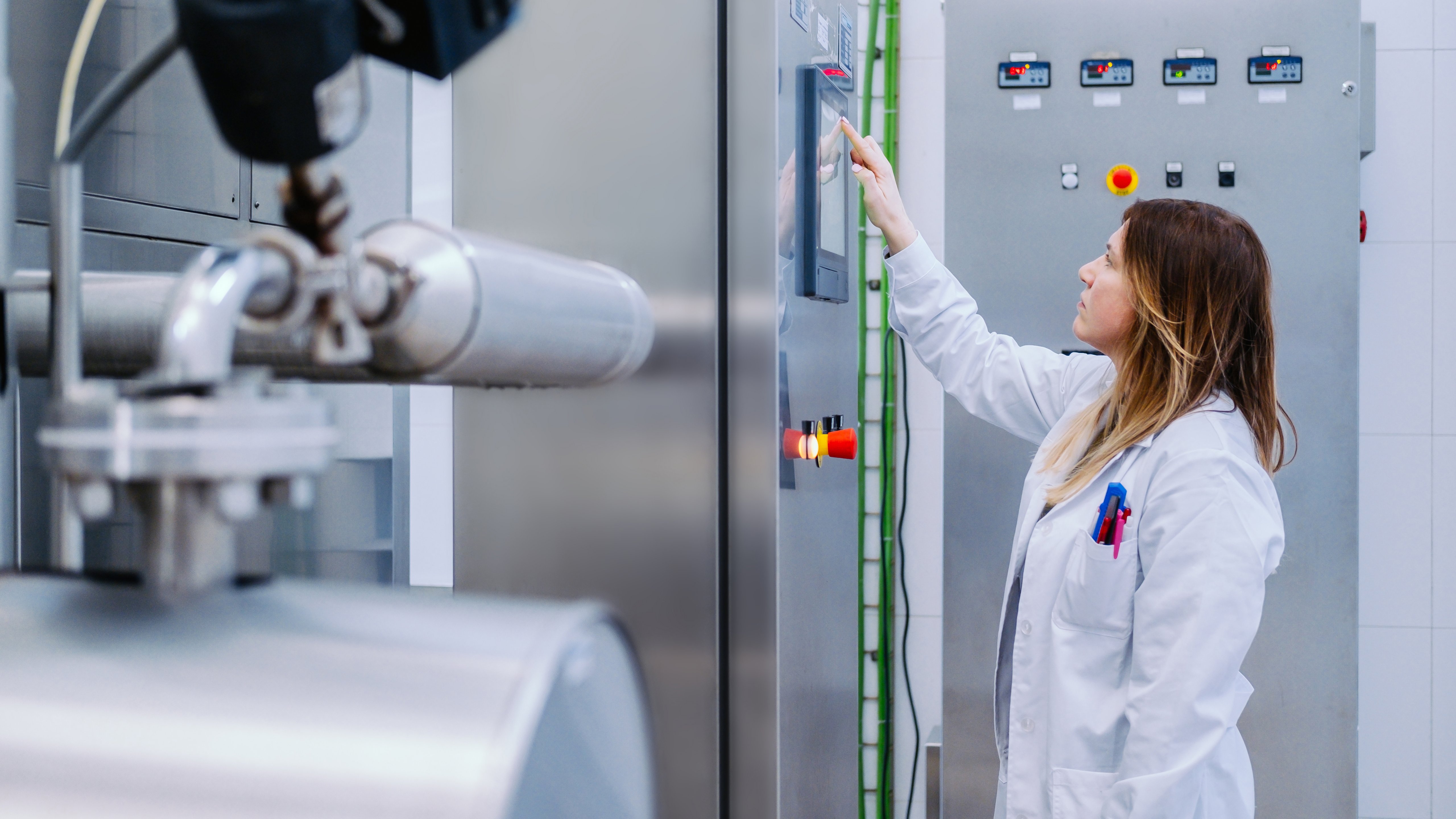 A female life sciences worker uses a digital screen on a large piece of equipment to check environmental conditions on the production floor.