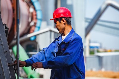 Single worker in blue jacket and red hardhat working with an asset on cement site