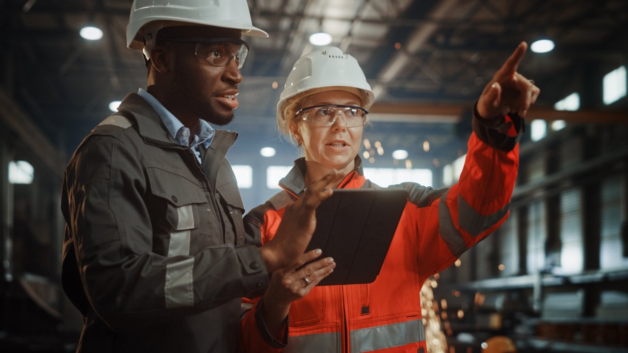 Co-workers discuss IT and OT convergence while viewing a handheld device that uses industrial network solutions for connectivity