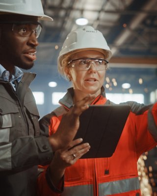 Co-workers discuss IT and OT convergence while viewing a handheld device that uses industrial network solutions for connectivity