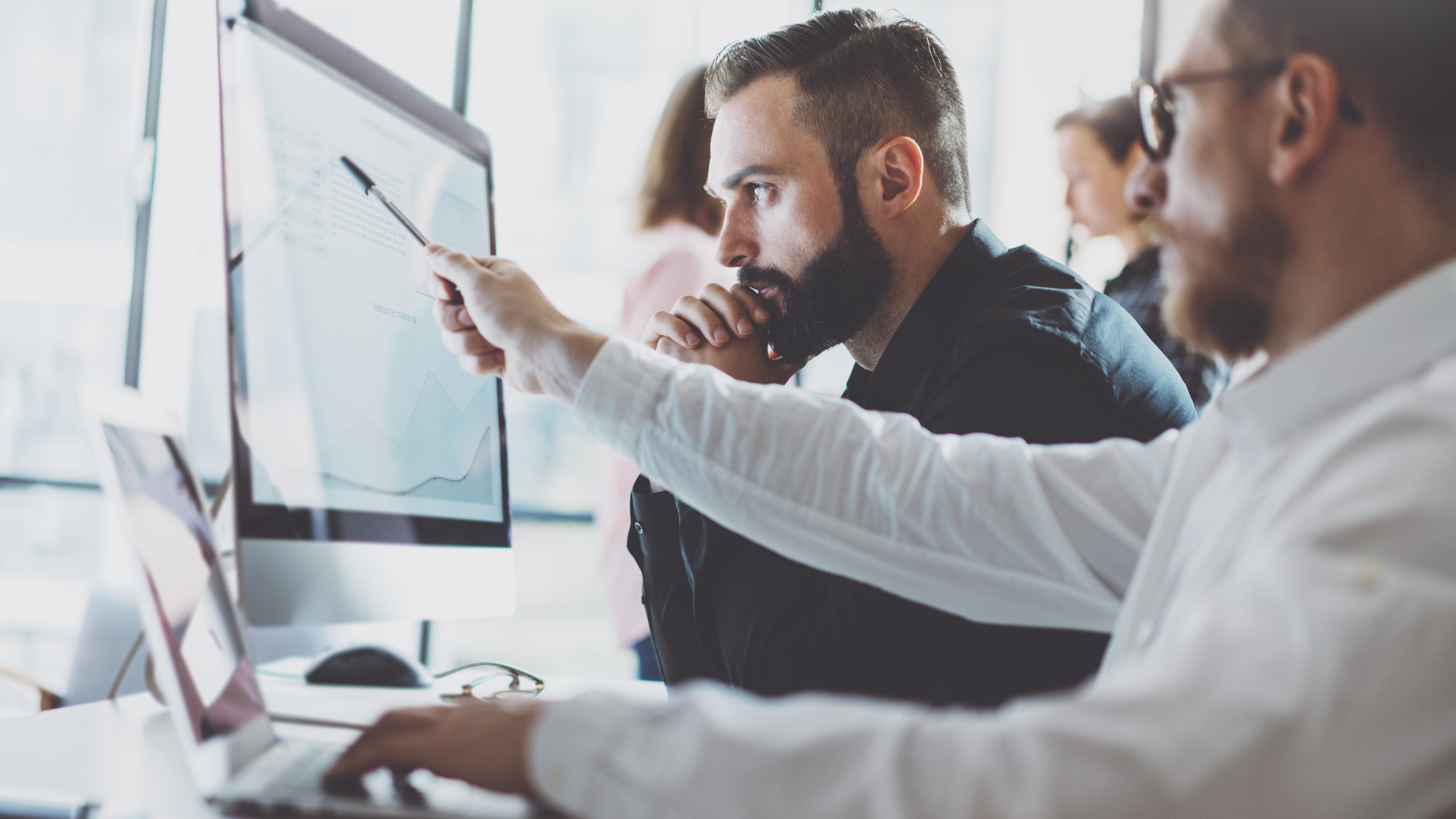 Focus is on two male employees viewing monitor with data