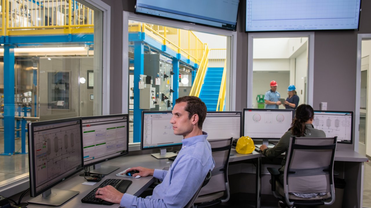 Un empleado que observa las métricas en su monitor sentado junto a otro compañero que evalúa los datos en una oficina separada con ventanas