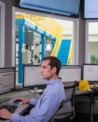 Ein Mitarbeiter sieht sich die Messdaten auf seinem Monitor an, während ein anderer Mitarbeiter die Daten in einem anderen Büro mit Fenstern auswertet