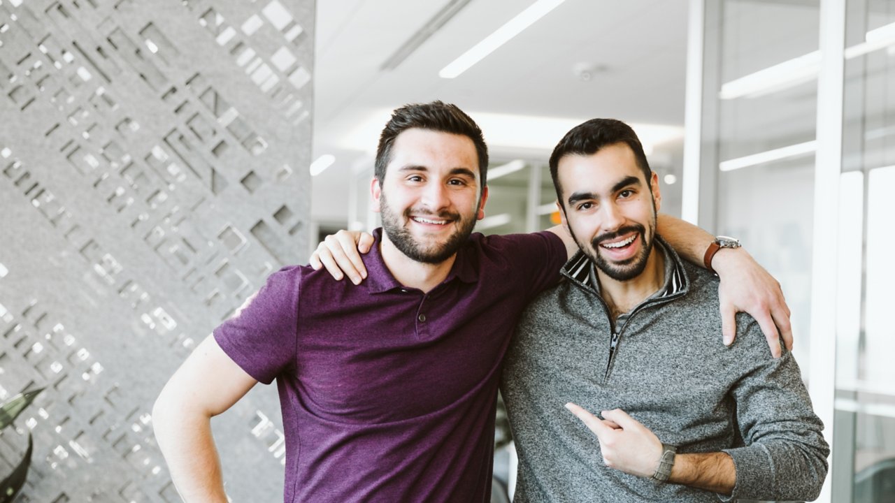 Two young men coworkers embrace casually in an office setting at Rockwell Automation