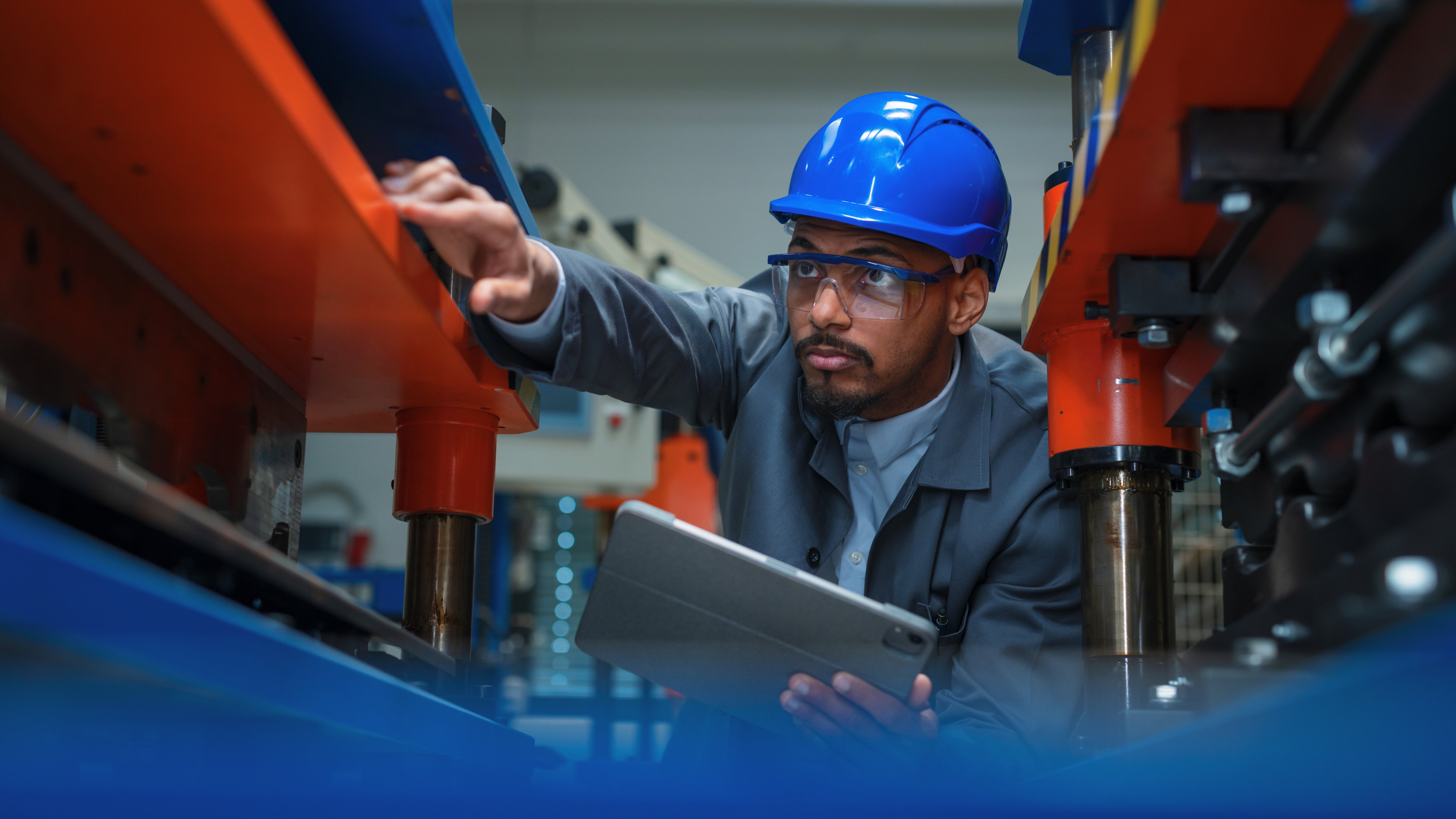 Engineer, with a blue helmet and safety glasses, checking manufacturing machinery, regulating the automatization process on a tablet, close up shot.