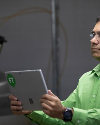 Male employee wearing a green shirt and safety glasses holding a tablet with a green FactoryTalk logo assessing process data