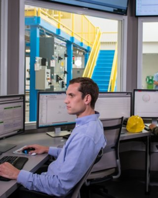 Ein Mitarbeiter sieht sich die Messdaten auf seinem Monitor an, während ein anderer Mitarbeiter die Daten in einem anderen Büro mit Fenstern auswertet 
