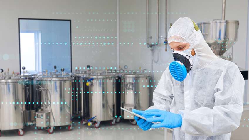 Worker wearing coverall and respirator using digital tablet in pharmaceutical factory.