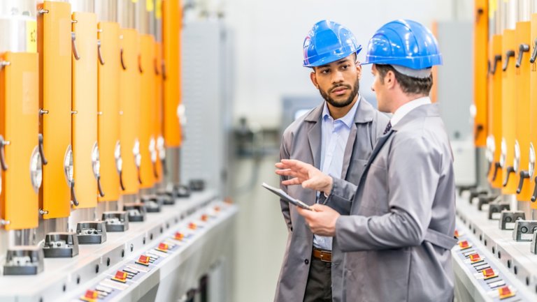 Two engineers talking while standing next to some machines in a factory.